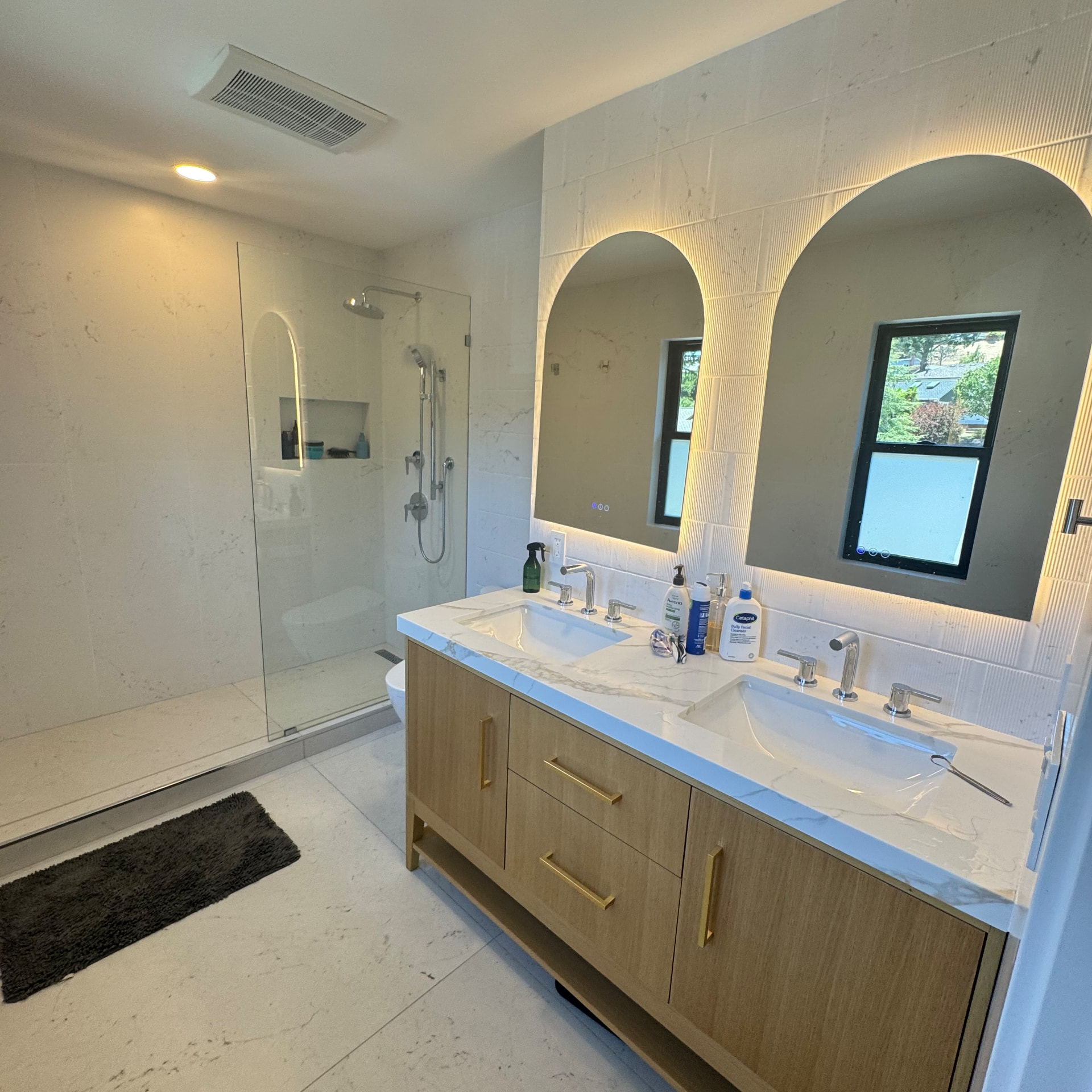 Modern bathroom with double vanity, arched mirrors, and glass walk-in shower